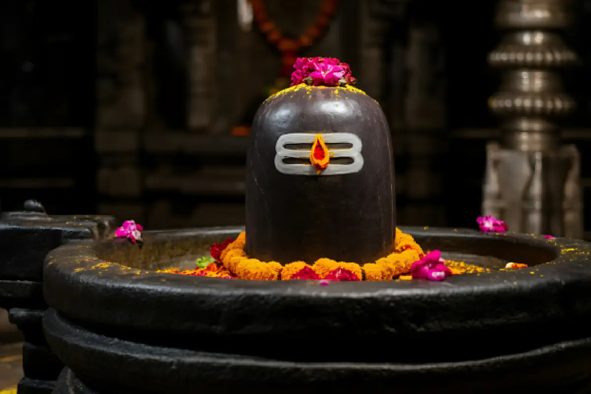 Black Shiva Lingam adorned with marigold flowers, symbolic of Lord Shiva worship in a Hindu temple.